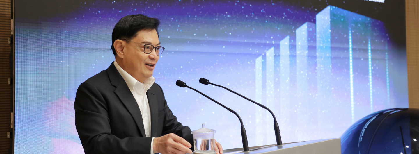 Man in suit at podium with two microphones. Background shows digital display with bar graph and stars.